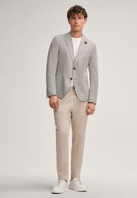 Gestreifter Blazer in Hellgrau und Weiß, kombiniert mit beigen Hosen und weißen Sneakers. Auffällige Merkmale: zwei Knöpfe, Taschen und Reversdetails.