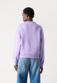 Felpa lilla con vestibilità comoda, spalle scese, polsini a costine e dettaglio nella cucitura posteriore, abbinata a pantaloni in denim chiaro.