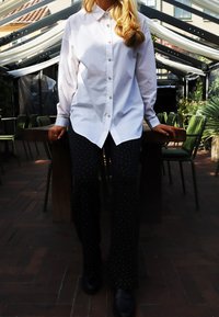 Valge pikkade varrukatega särk nööpidega, mida kannavad mustad püksid valgete täppidega. Stseenis on puidust laud ja rohelised toolid.