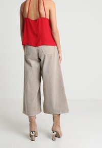 Top rosso senza maniche con spalline sottili abbinato a pantaloni beige a gamba larga. L'outfit presenta una vestibilità ampia e un tessuto texturizzato.