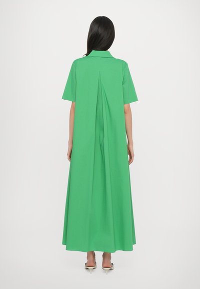 Zielona bawełniana sukienka maxi z krótkimi rękawami, kołnierzykiem i detalem w postaci zakładki z tyłu, swobodnie opływająca aż do ziemi. Minimalistyczny design.