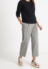 Černý svetr z vaflového úpletu, kostkované krátké kalhoty a barevné tenisky. Viditelná strukturovaná tkanina a výrazné barevné akcenty.