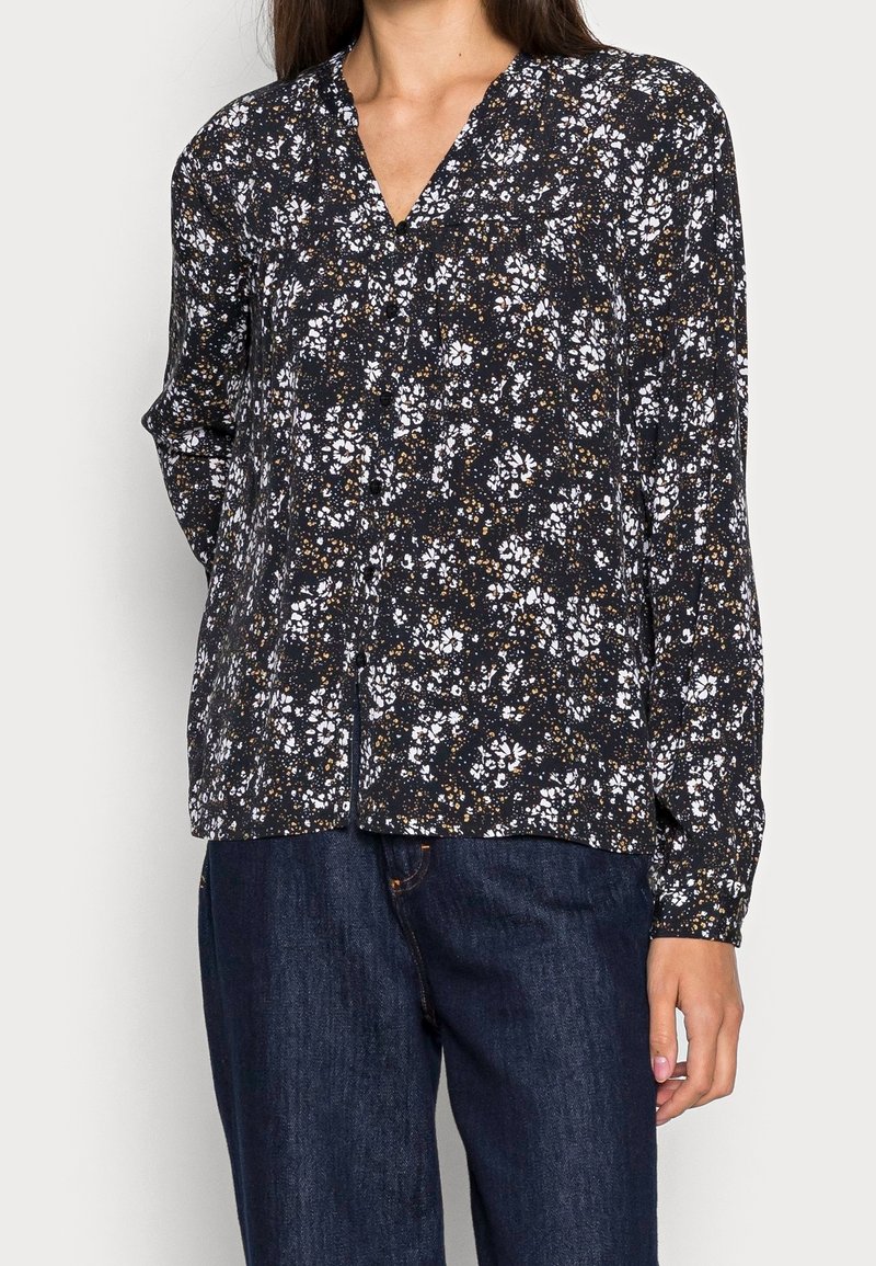 Musta paita, jossa valko- ja ruskeakukkainen kuvio, v-pääntie, pitkät hihat ja rento istuvuus. Valmistettu kevyestä kankaasta.