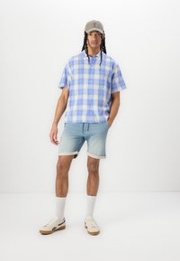 Short-sleeve, blue plaid shirt with a button-up design; light denim shorts, rolled cuffs; gray cap; cream sneakers with rubber soles.