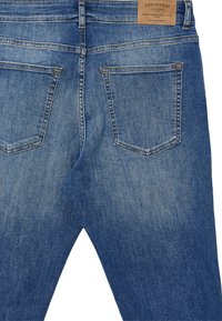Jeans in denim azzurro chiaro con effetto sbiadito, dotati di un'etichetta in pelle sulla cintura e due tasche posteriori con dettagli di cucitura.