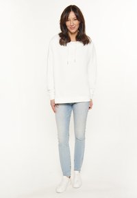 Witte hoodie met koordjes, gecombineerd met lichtblauwe skinny jeans en witte sneakers. Glad stofgevoel, casual pasvorm.