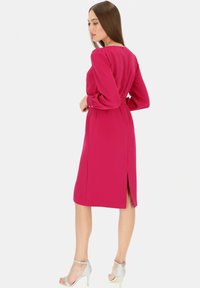 Fuksjowa midi sukienka z długimi rękawami, okrągłym dekoltem, dopasowaną talią i rozporkiem z tyłu. W zestawie ze srebrnymi sandałami na obcasie.