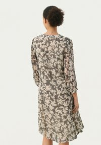 Blumenmuster, halbtransparentes Kleid mit drei Viertel Ärmeln, hellem beigen Grundton und dunklen Akzenten, im entspannten Schnitt und knielanger Länge.