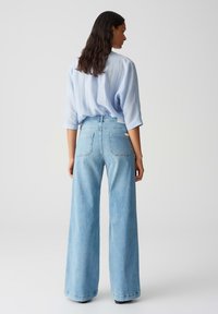 Light blue oversized shirt with rolled sleeves, paired with wide-leg light blue denim jeans featuring back pockets and a high waist.