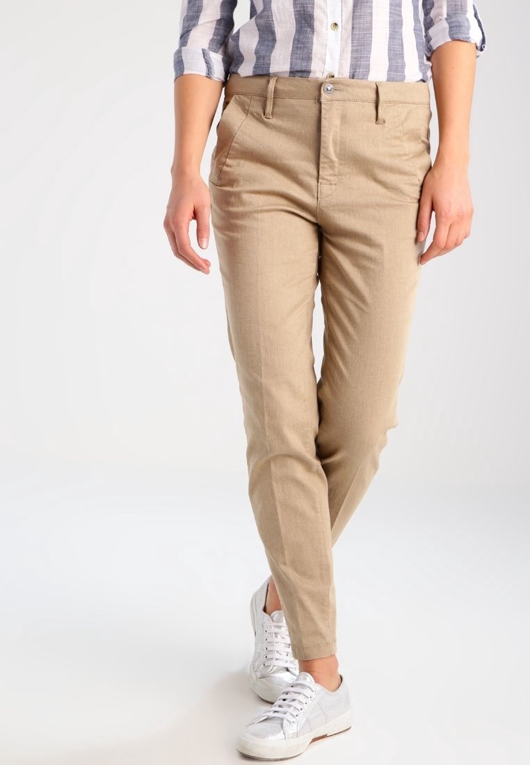 Khaki slim-fit housut, jotka on valmistettu pehmeästä kankaasta; varustettu etutaskuilla, napilla suljettuna ja sileällä pinnalla. Yhdistetty valkoisiin lenkkareihin.