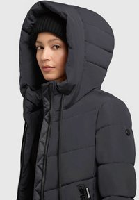 Puchowa czarna kurtka z dużym kapturem, zapięciem na zamek błyskawiczny i ściągaczami. Posiada pikowaną teksturę i boczne kieszenie, w komplecie z dzianą czarną czapką.