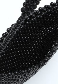 Borsa a mano nera con superficie texturizzata, forma arrotondata e manico di perline, caratterizzata da elementi sferici uniformi in tutto il design.