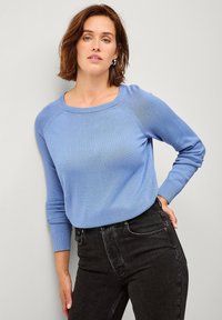 Lichtblauwe trui met een ronde hals en lange mouwen, gemaakt van zachte stof, gecombineerd met zwarte jeans. Subtiele textuur en aansluitend ontwerp.