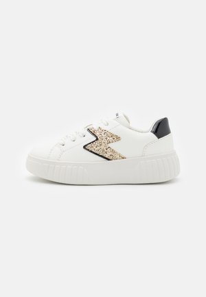 Baskets blanches avec un design éclatant de lightning bolt doré, accents noirs, semelle en caoutchouc texturé et lacets ronds. Matériau synthétique lisse.