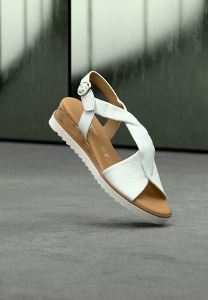 Weiße Ledersandale mit überkreuzten Riemen, Kork-Zwischensohle und weißer Gummisohle. Mit einem silbernen Schnallendetail am Knöchelriemen.