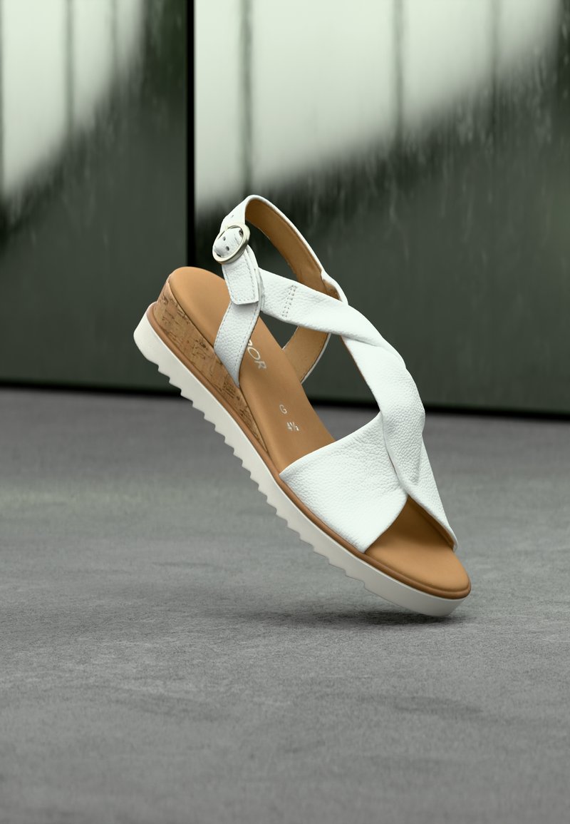 Λευκό δερμάτινο σανδάλι με σταυρωτούς ιμάντες, μεσαία σόλα από φελλό και λευκή λαστιχένια σόλα. Διαθέτει ασημένια αγκράφα στη λουράκι του αστραγάλου.