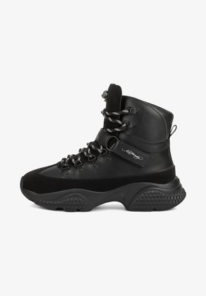 Bota deportiva negra de caña alta con suela gruesa y texturizada, cordones negros y blancos, cierre de velcro y logo en el lateral.