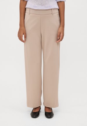Beige, vide bukser med glat tekstur, der har en mid-rise talje og sidelommer. Sammen med sorte flade sko.