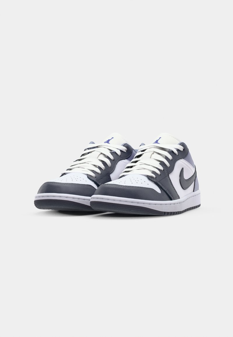 Sneaker basse con tomaia bianca, dettagli in pelle grigio scuro, punta perforata, lacci bianchi e un logo blu sulla linguetta. Suola in gomma.