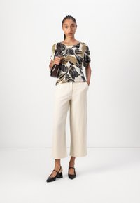 Top a maniche corte con motivo floreale in beige, nero e oliva; abbinato a pantaloni larghi a vita alta in crema e décolleté nere con cinturino. 