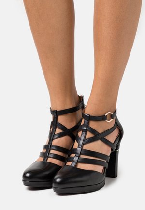 Chaussures à talons hauts noires en cuir, avec plusieurs lanières, un bout fermé et un talon bloc avec un détail de bride géométrique à la cheville.