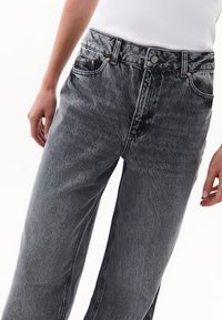 Jeans de mezclilla gris de cintura alta con un acabado ligeramente desgastado, diseño de pierna recta, cinco bolsillos y acentos de herrajes de cobre.