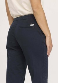 Pantalons en coton bleu marine à coupe droite, avec des poches arrière et une petite étiquette de logo sur la taille pour l'identification de la marque.