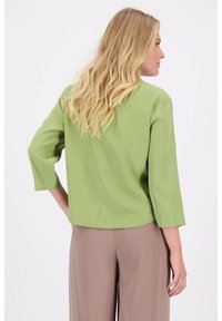 Groene, lichte blouse met driekwart mouwen, een soepele textuur, ronde zoom en eenvoudig ontwerp, gecombineerd met beige wijde broeken.