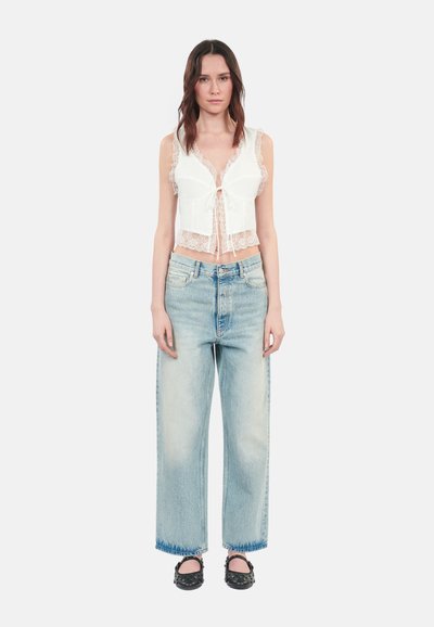 White lace-trimmed top with a tie front, paired with light blue wide-leg jeans. The outfit features a casual fit and a textured appearance.
