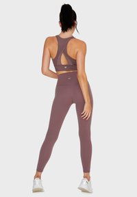 Mockingbark sportbeha in mauve met uitgesneden achterkant ontwerp, gecombineerd met bijpassende hoge taille leggings. Soepele, rekbare stof. Witte sneakers.