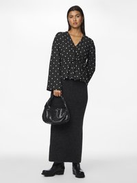 Mustvalge ruuduline pluus V-kaelusega ja lipsu ees, koos halli kudumisega maxi seelikuga ja mustade kontsaga saapatega; hoiab käes läikivat musta kotti.