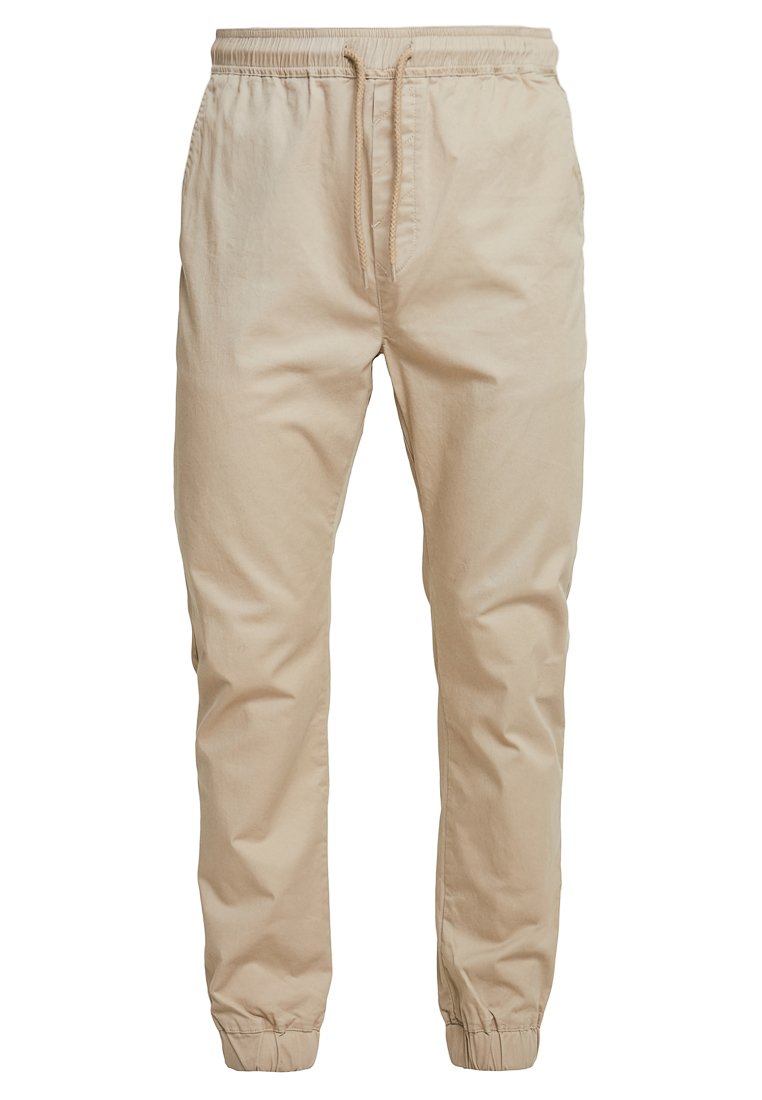 Beige jogger pants made of woven fabric, featuring an elastic waistband with drawstring, side pockets, and elastic cuffs at the ankles.