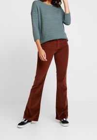 Grönrandig stickad tröja med båtenskärning. Rostfärgade manchesterbyxor med utsvängd ben. Svarta och vita sneakers. Enkel, avslappnad outfit.