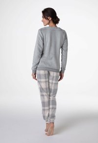 Felpa grigia in pile con polsini a coste, abbinata a pantaloni a quadri in grigio, bianco e rosa. Tessuto morbido e vestibilità comoda.