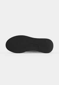 Semelle de chaussure en caoutchouc noir avec une accroche texturée et un insert rectangulaire affichant le nom de la marque « BOSS » au centre.