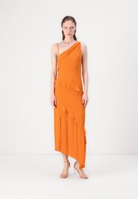 Orange asymmetrisk klänning i mjukt tyg, med volangdetaljer och en slits upp till låret. Kombinerad med nakna remsandaler.