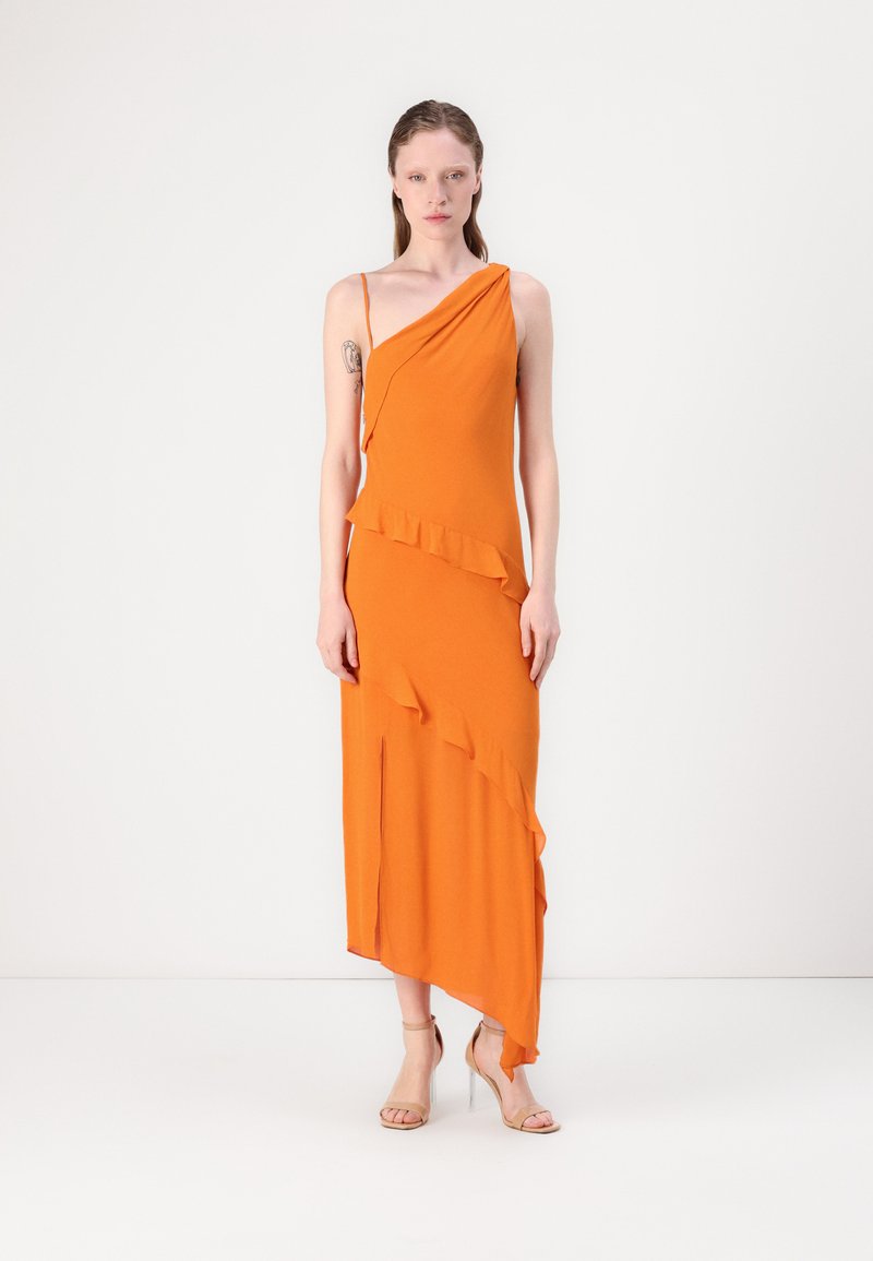 Orange asymmetrisk klänning i mjukt tyg, med volangdetaljer och en slits upp till låret. Kombinerad med nakna remsandaler.