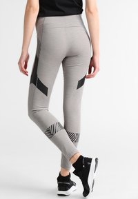 Leggings gris avec une taille haute, ornés de motifs géométriques noirs et de bandes au bas des jambes, fabriqués dans un tissu lisse et extensible.