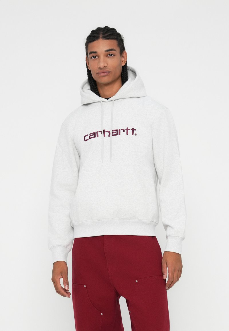 Felpa grigia con tasca a canguro frontale e cordini, con il logo "carhartt" color bordeaux. Abbinata a pantaloni bordeaux con tasche laterali.