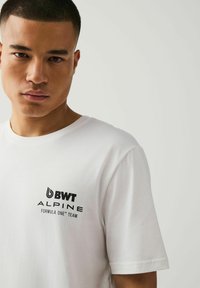 Bela bomba iz bombažnega materiala z natisnjenim črnim logotipom, ki vsebuje "BWT ALPINE" in "FORMULA ONE™ TEAM" na levi strani prsnega dela. Klasika z krožnim izrezom.