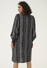 Rochie cu model alb și negru, cu mâneci bufante, croială lejeră și tiv până la genunchi, cu o textură netedă și moale.
