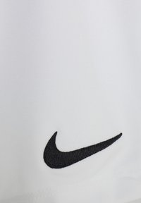 Tela blanca con una textura suave que presenta el logotipo de Nike bordado en negro. Perspectiva cercana que se centra en los detalles del logotipo y del material.