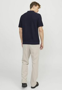 Polo navy a maniche corte, colletto e orlo ribattuto, abbinato a pantaloni beige e scarpe scure, visto da dietro.