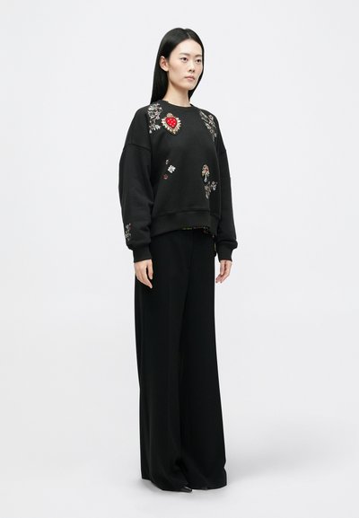 Musträd must sweatshirt lille ja südame tikandiga, koos laia musta pükstega. Omab vabalt langemist ja soonikkoes varrukaotsasid.