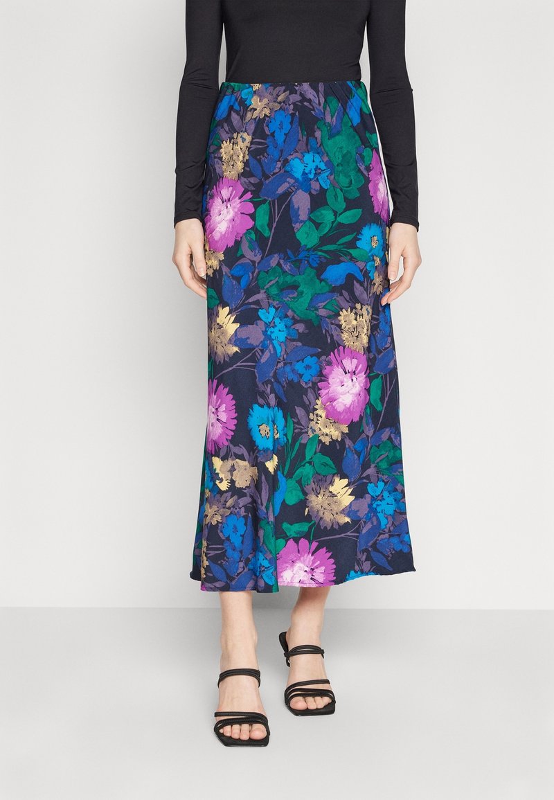 Jupe longue fleurie avec un fond bleu marine orné de fleurs vibrantes en violet, bleu, vert et or. Associée à des sandales noires à brides.