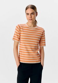 Top a maniche corte a righe in arancione chiaro e crema, con scollatura tonda e texture a coste, abbinato a pantaloni neri.