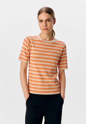Randig kortärmad topp i ljus orange och kräm, med rund halsringning och ribbad struktur, i kombination med svarta byxor.