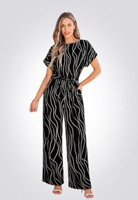 Combinaison ample noire à jambes larges avec des lignes ondulées blanches, manches courtes et ceinture à nouer. Fabriquée dans un matériau doux avec une texture lisse.