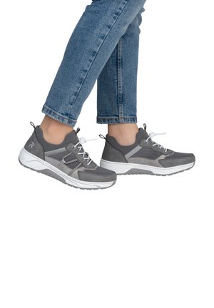 Person wearing gray and white athletic sneakers paired with blue jeans, standing with one foot slightly raised.