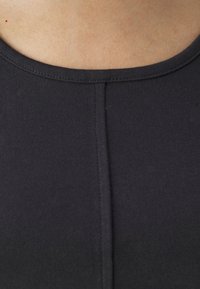 Gros plan d'un haut en tissu noir avec une couture verticale centrale et un col rond sur une peau claire.